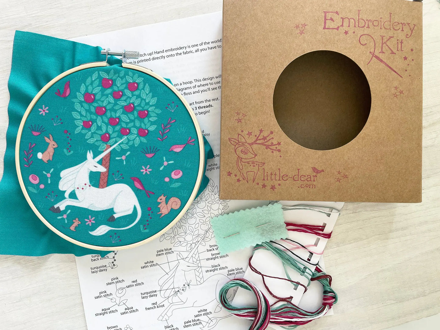 Embroidery kit with hoop, fabric, threads, and instructions on a wooden surface.