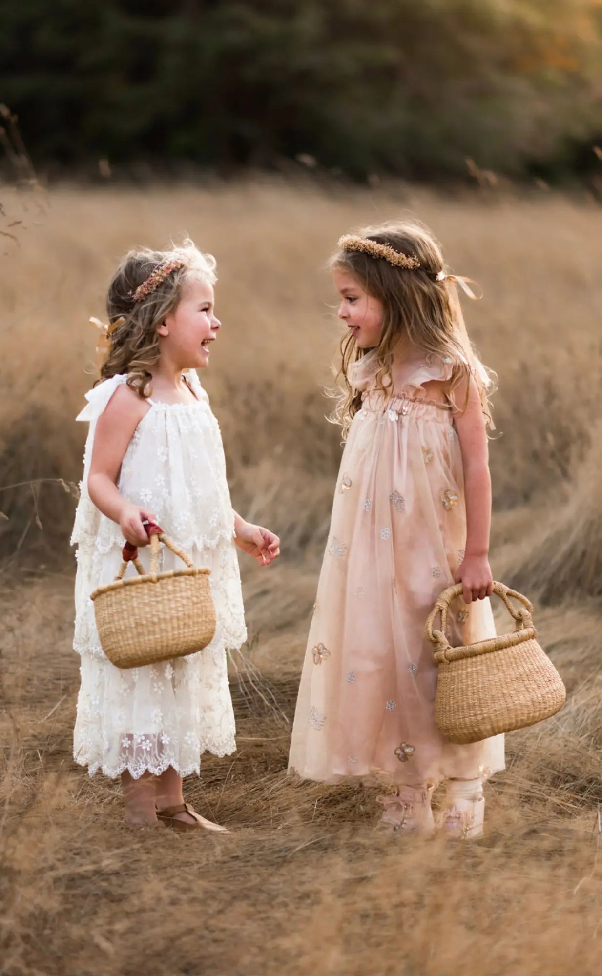 Two young girls in dresses standing in a field holding baskets.