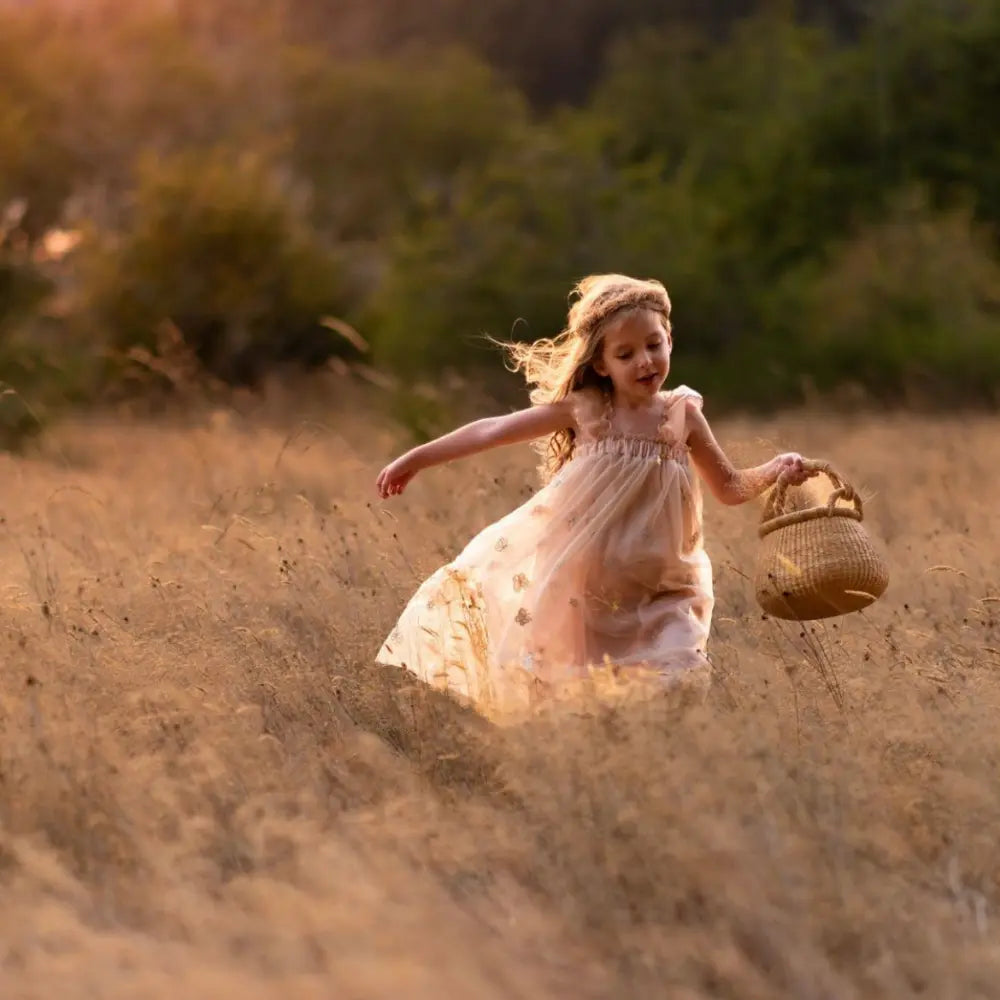 Young girl running through a field with a basket at sunset