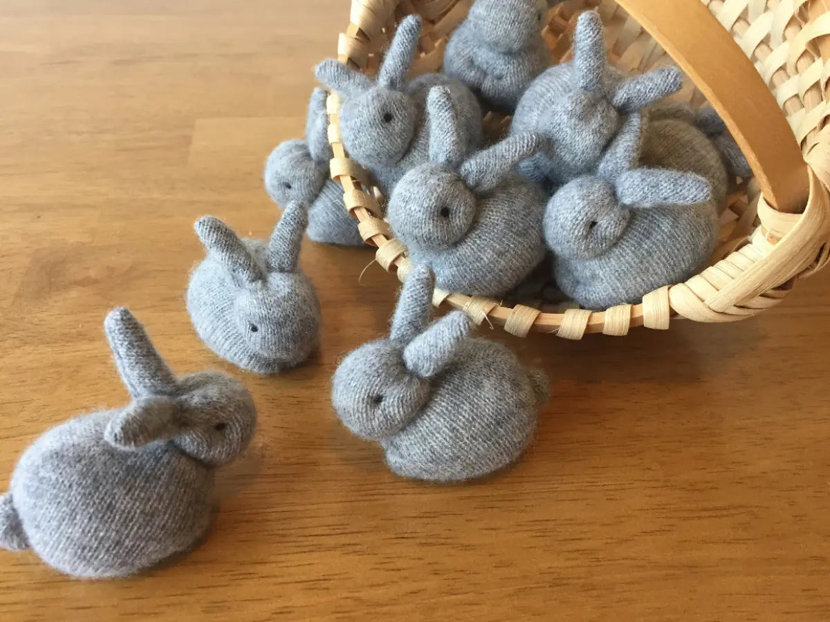 Gray knitted bunnies with a wicker basket on a wooden surface