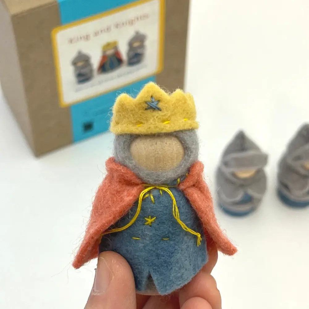 Handmade felt king toy with a crown and cape held in front of a book and other toys.