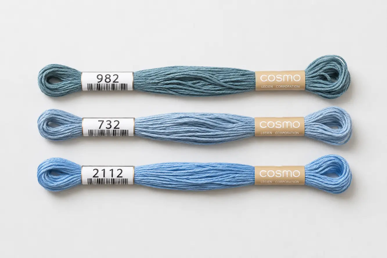Three skeins of blue embroidery floss with labels on a white background, branded 'Cosmo'.