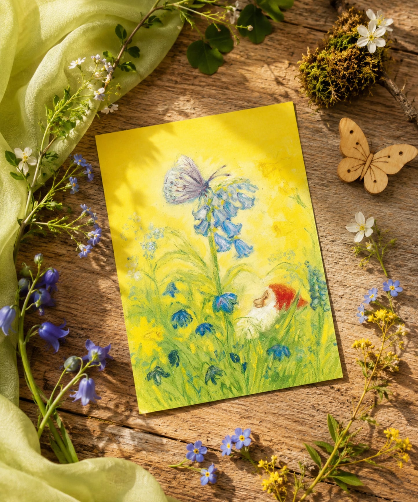 Gnome and butterfly illustration on a yellow card with flowers and nature elements on a wooden surface