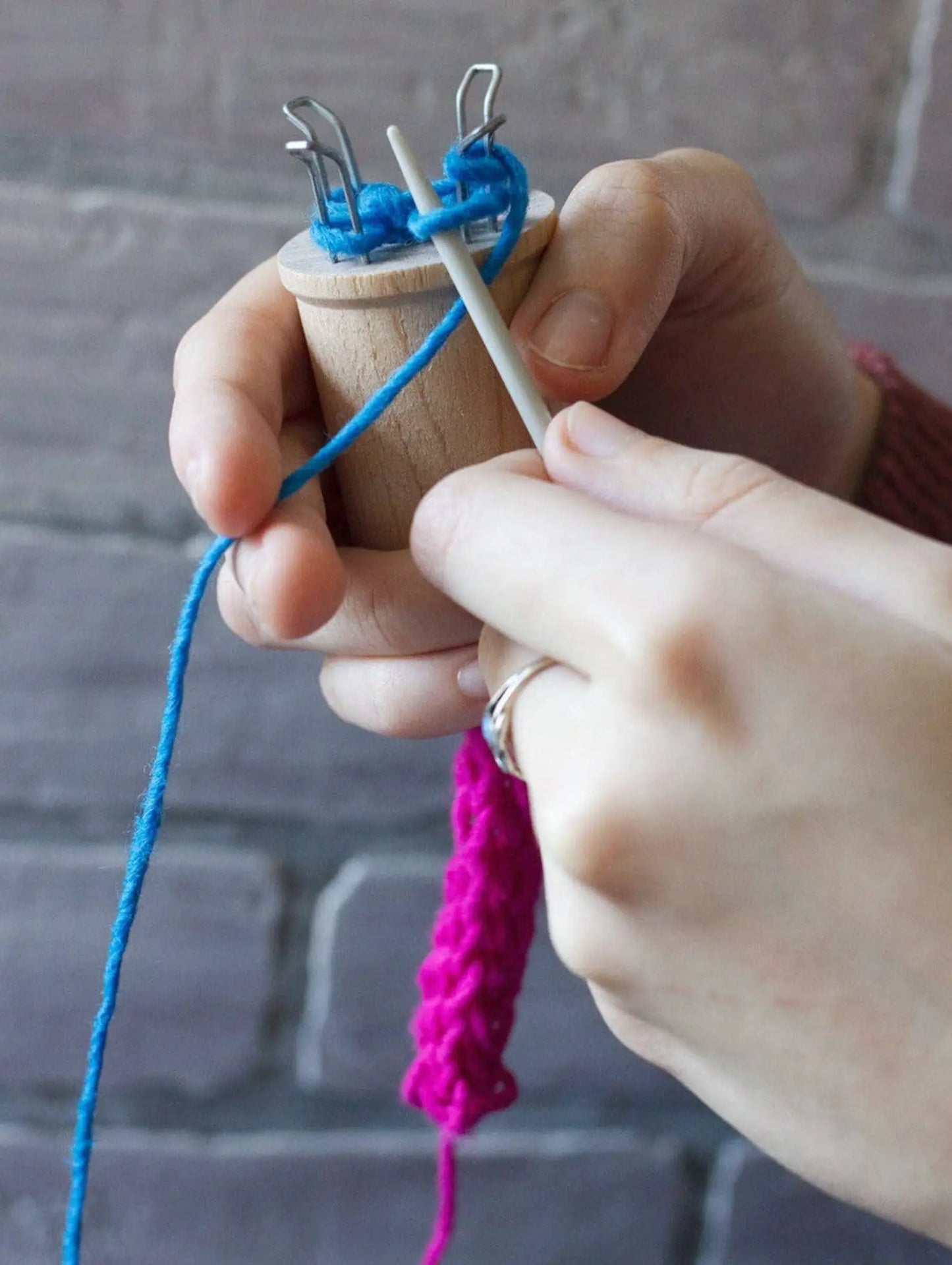 Close-up of hands knitting with blue yarn and a pink knitted item.