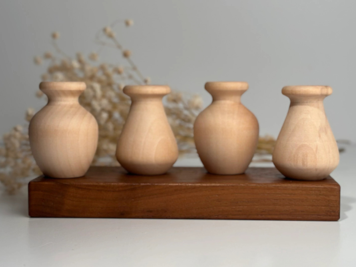 Four wooden vases on a wooden stand with a blurred floral background