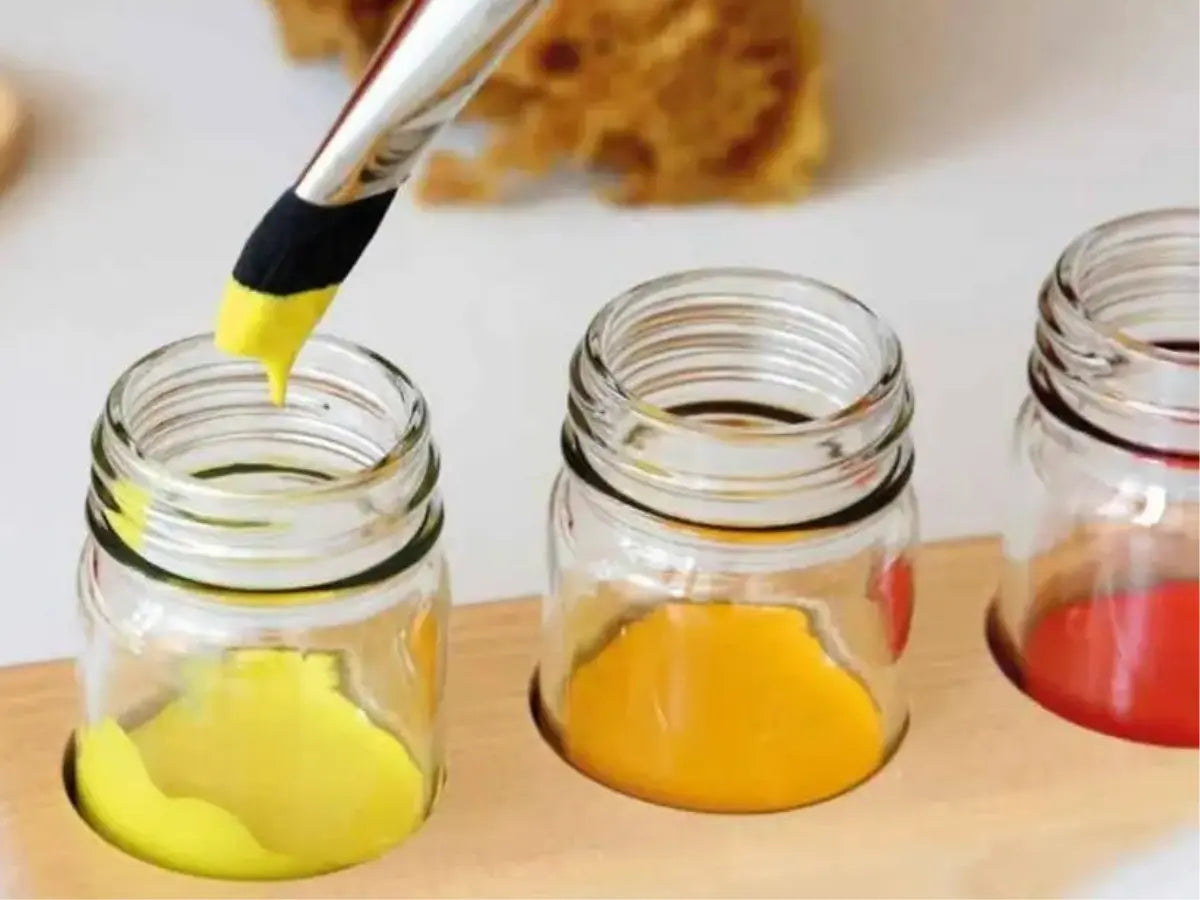 Glass jars with colorful watercolor liquids and a paintbrush 