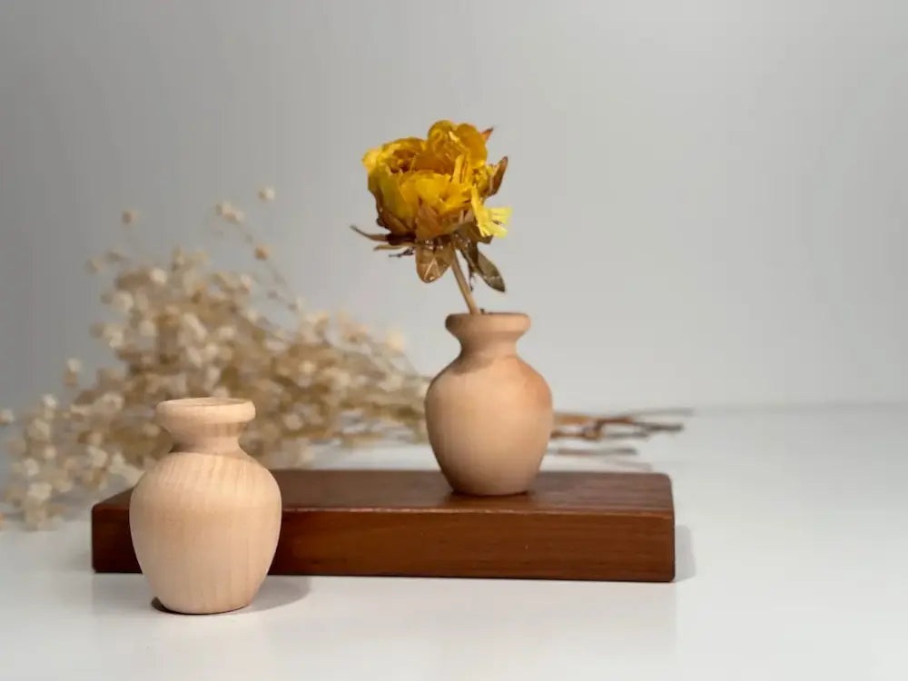 Two small wooden vases with yellow flowers on a white surface