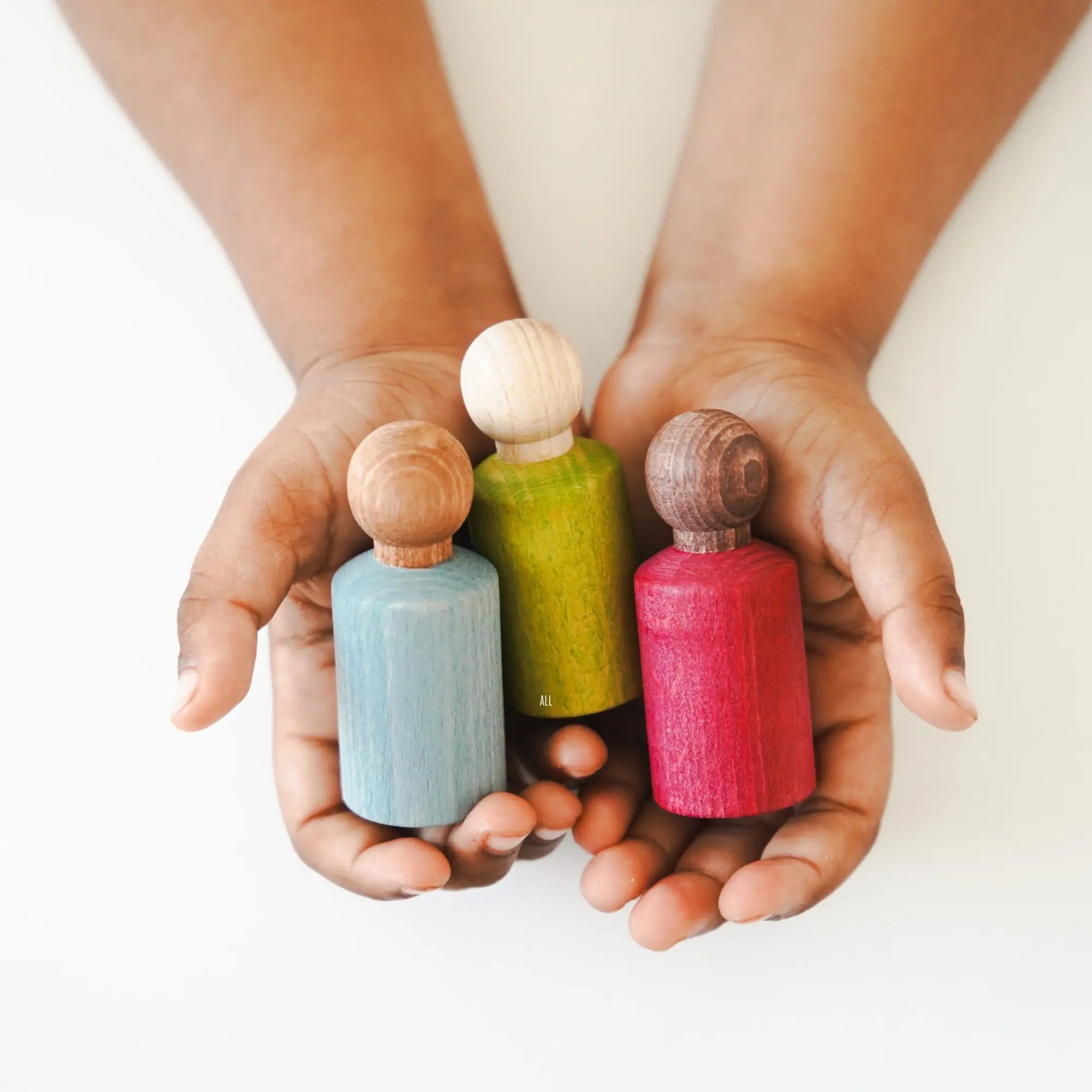 Three small wooden waldorf peg doll toys held in hands against a white background
