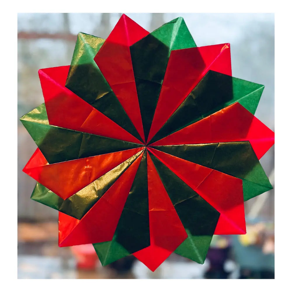 Waldorf kite paper window star folded into geometric shapes with red, green, and gold colors on a blurred background