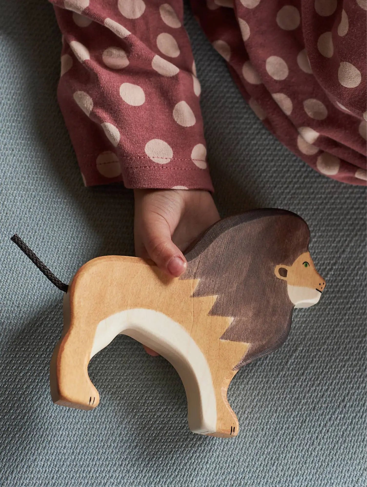 Wooden lion toy held by a child's hand with polka dot sleeves on a soft surface