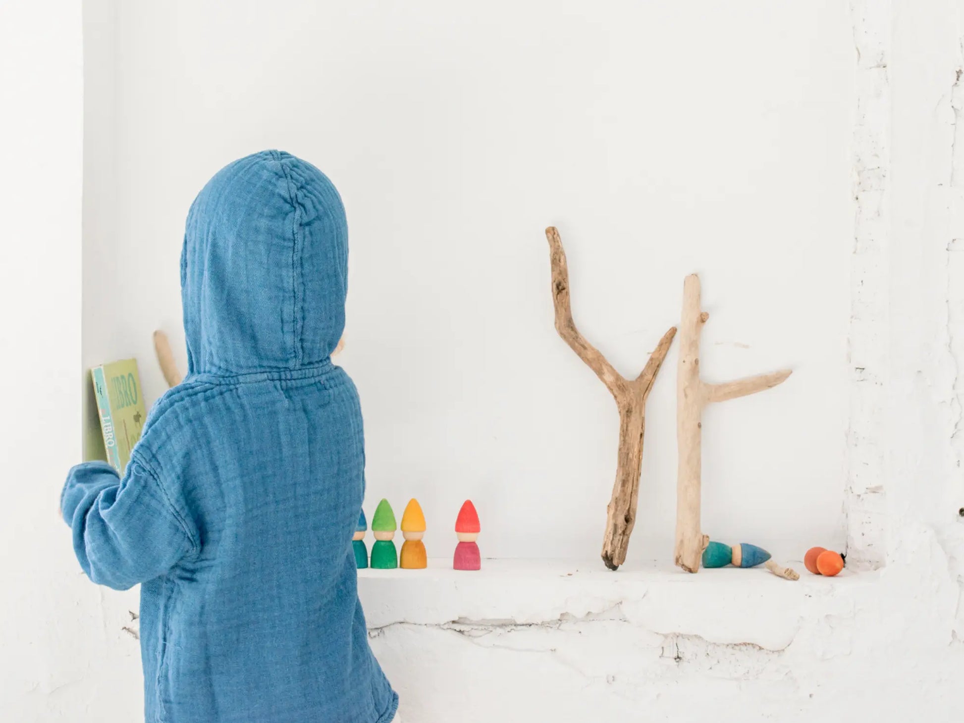 Child in a blue hooded towel standing in front of a wall with colorful letters made from sticks.