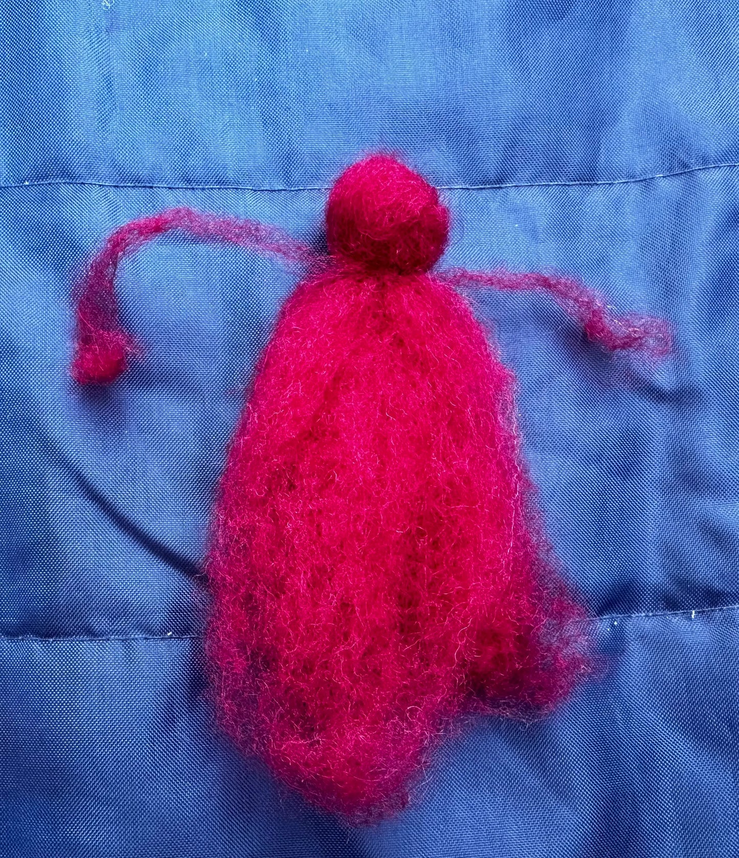 close up of wool fairy doll in progress in red on blue background