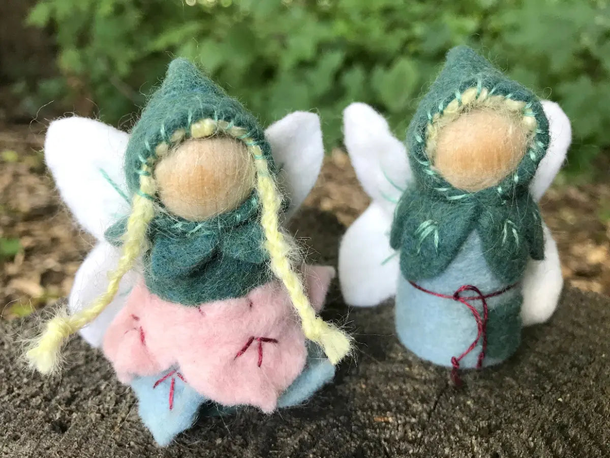 Two small fairy figures on a natural surface with greenery in the background