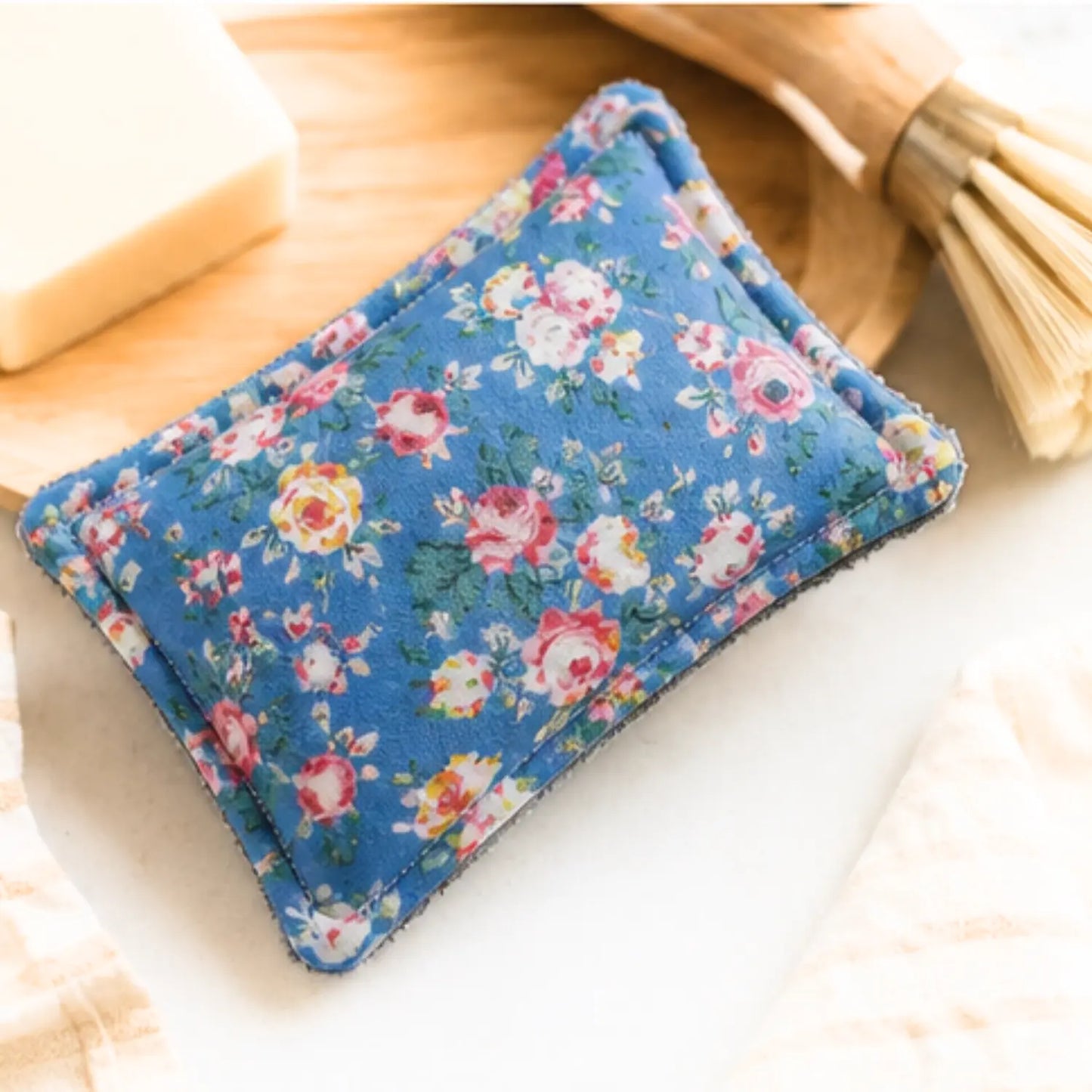 Blue floral washable sponge beside bar soap and a dish brush in a kitchen setting