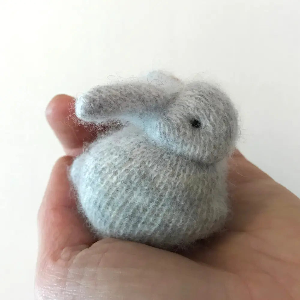 Small cashmere knitted bunny held in a hand against a white background