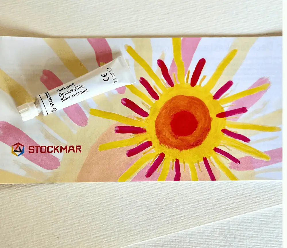 Tube of Stockmar paint with a colorful sun drawing on a white background