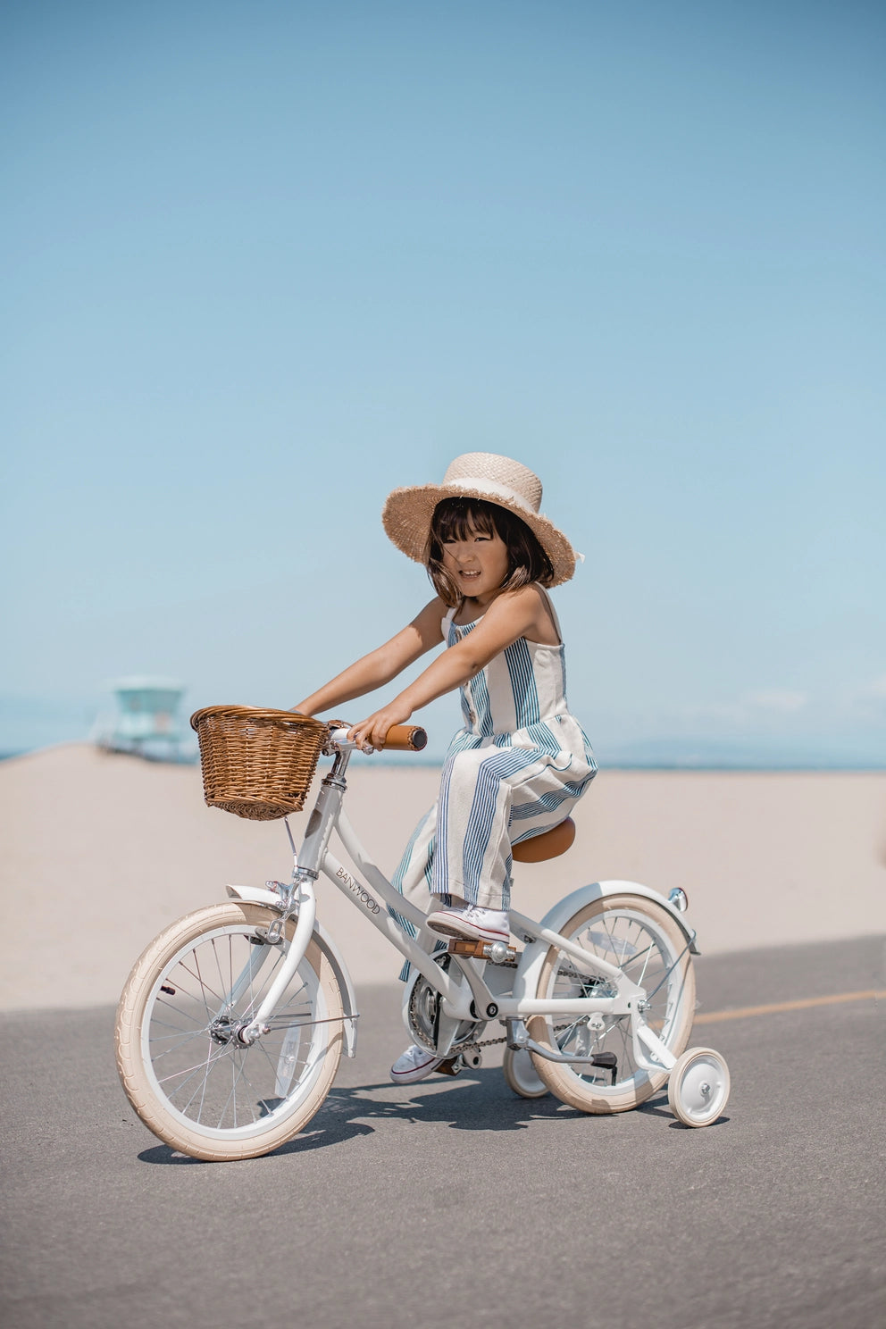 Child riding a Banwood bicycle with a basket and training wheels on a clear day