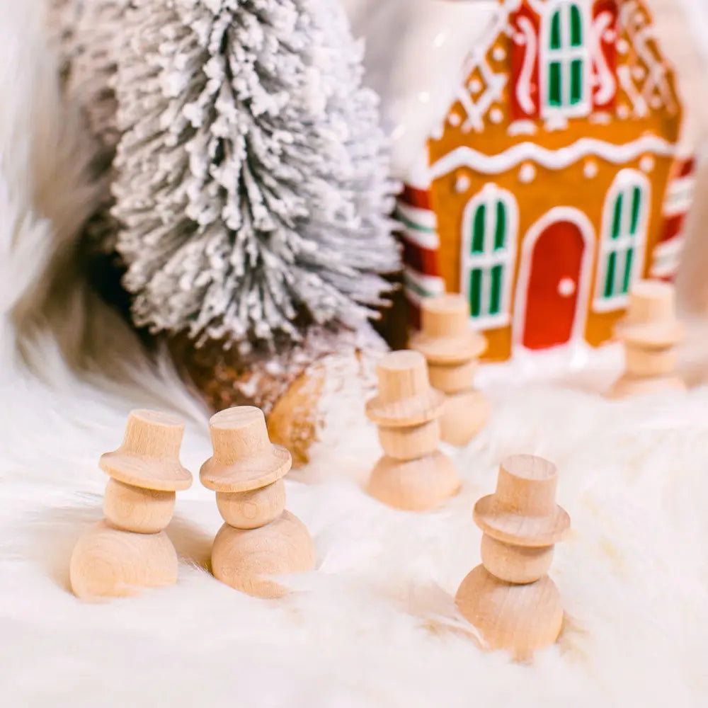 Wooden snowmen figures in front of a gingerbread house and snowy tree