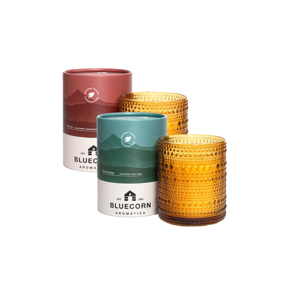 Three candles with different designs and a branded container on a white background