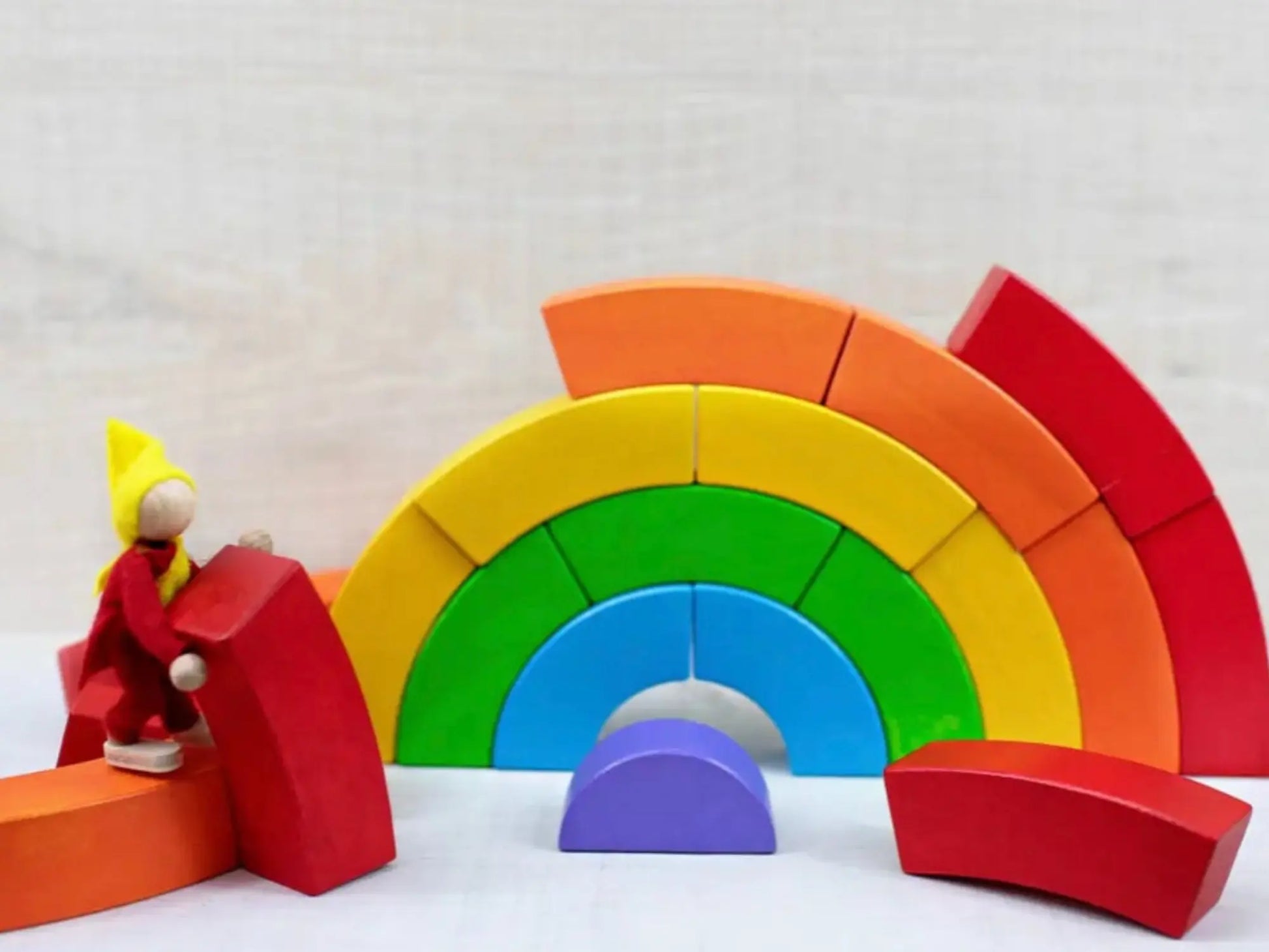 Colorful wooden rainbow toy with a small figure on a white background