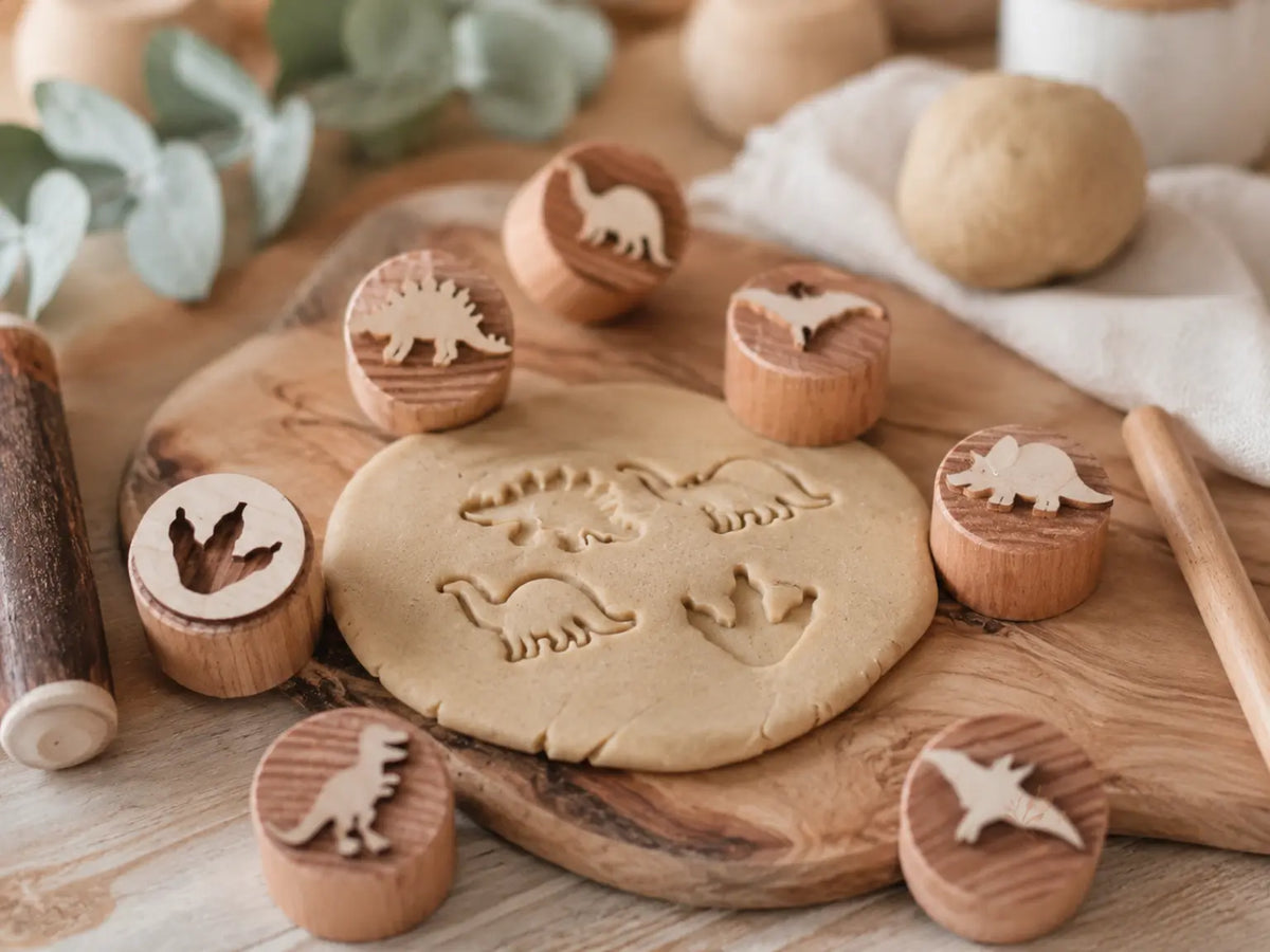 Wooden dinosaur stamps arranged around natural play dough with dinosaur impressions