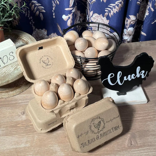 Wooden eggs in a cardboard carton on a wooden surface with a decorative sign in the background.