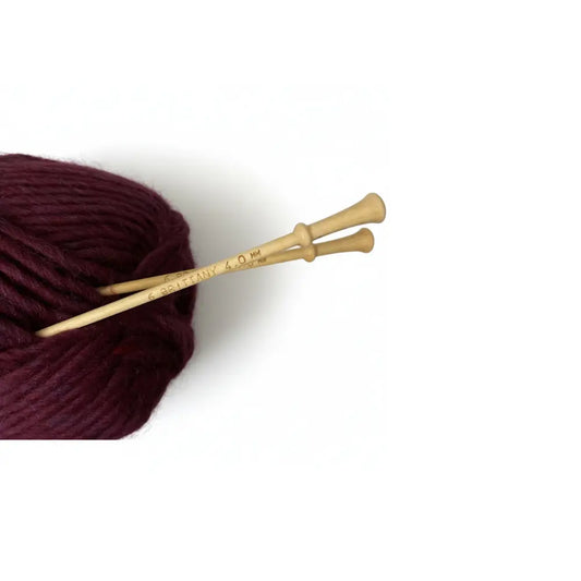 Maroon yarn ball with wooden knitting needles on a white background