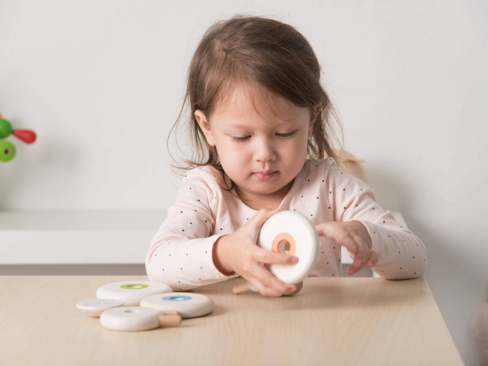 Child playing with wooden sheep lacing toys on a table