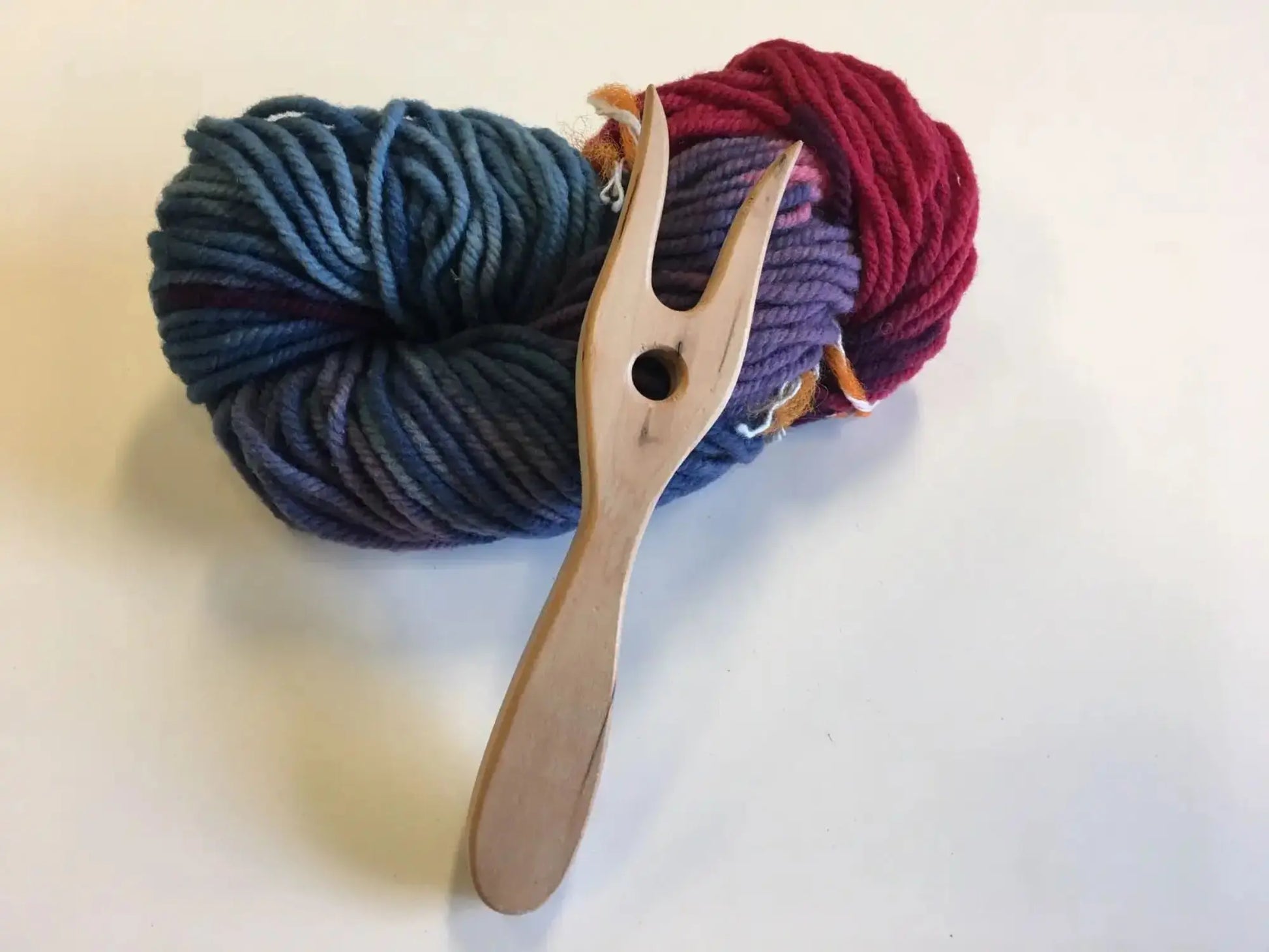 A wooden lucet for kids on top of a hank of wool rainbow yarn in blue, liliac, pink and red