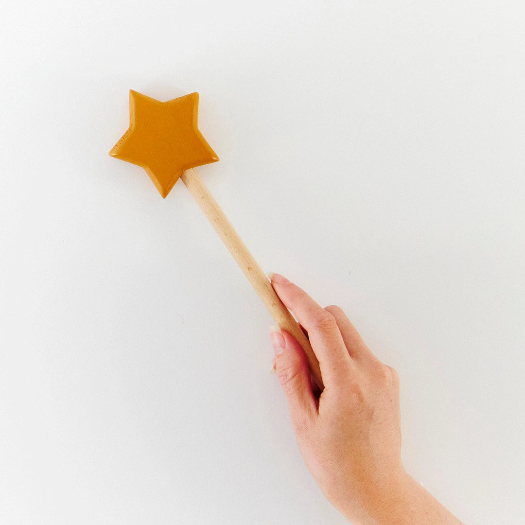 Hand holding a star-shaped wooden toy wand for imaginary play on a white background