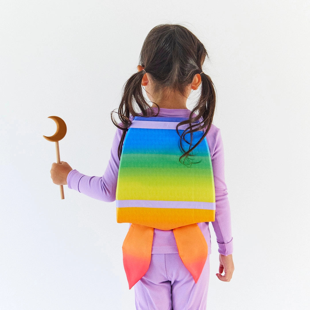 Child holding wooden magic wand during dress up play with rainbow backpack