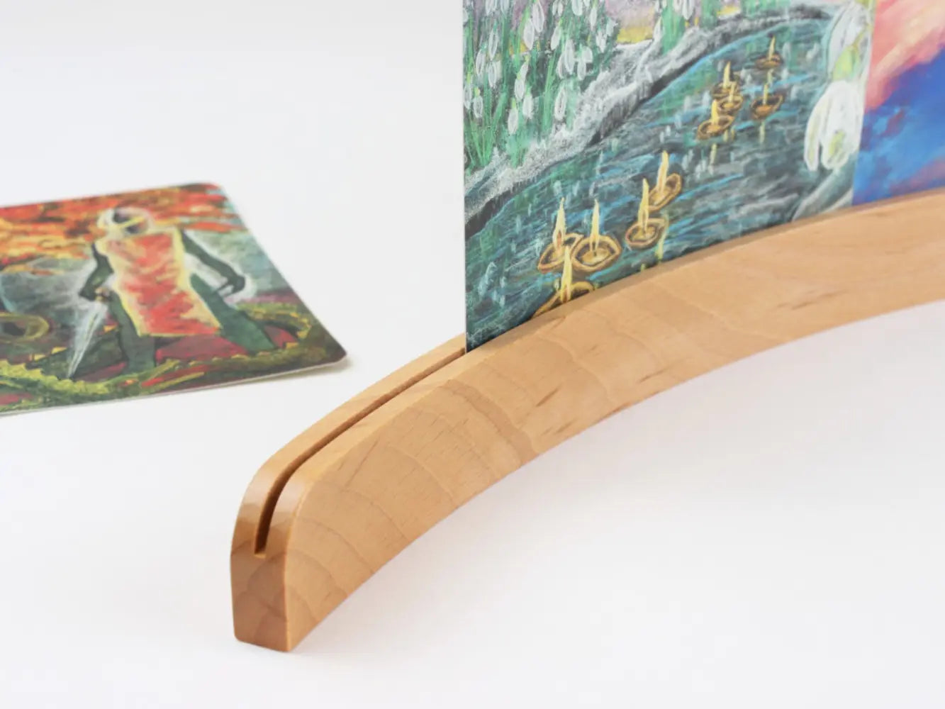Close-up of a curved European beechwood postcard holder showing the card slot and seasonal art postcard display detail.