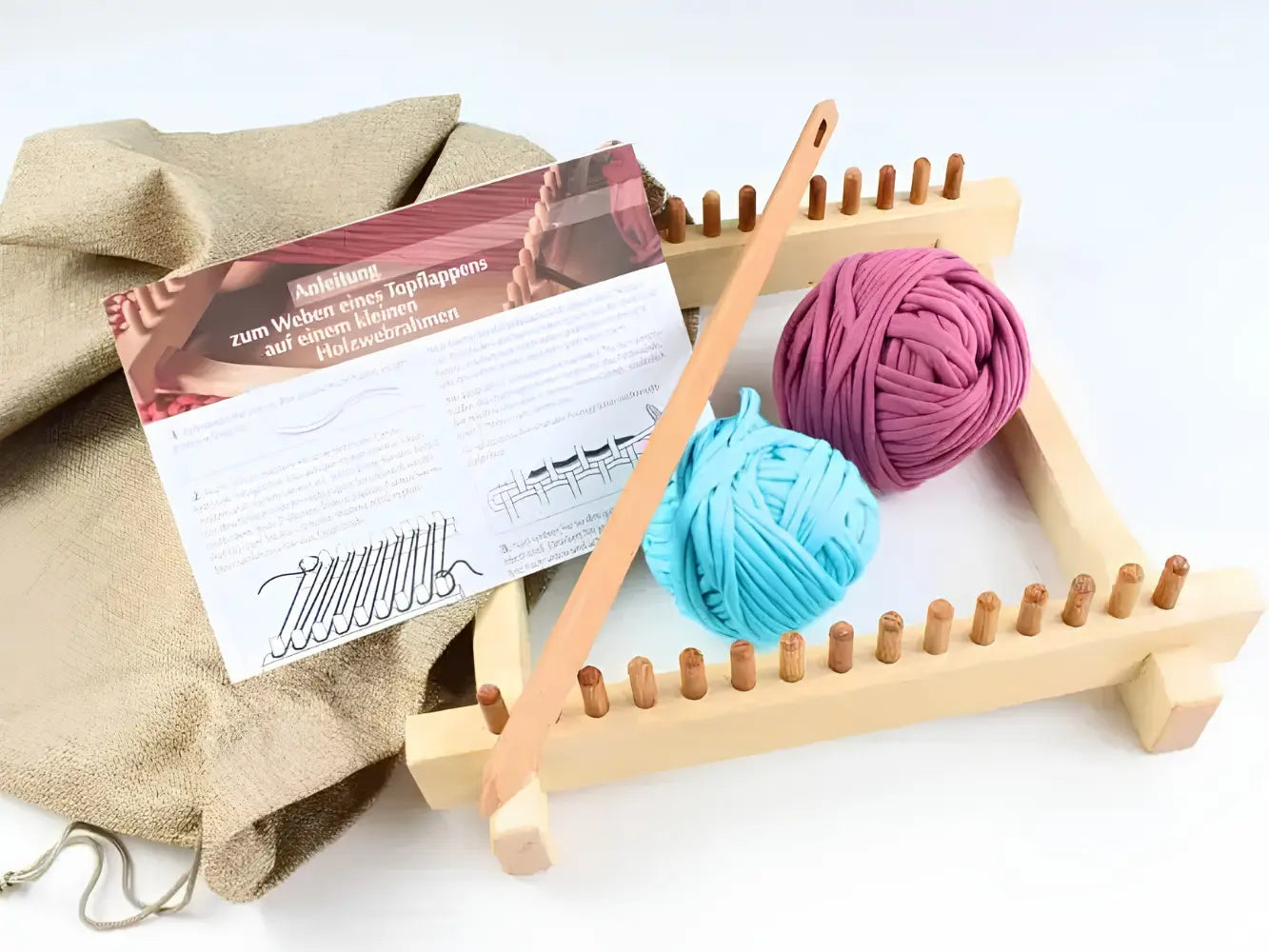 Wooden pot holder loom with two balls of yarn and a pattern sheet on a white background