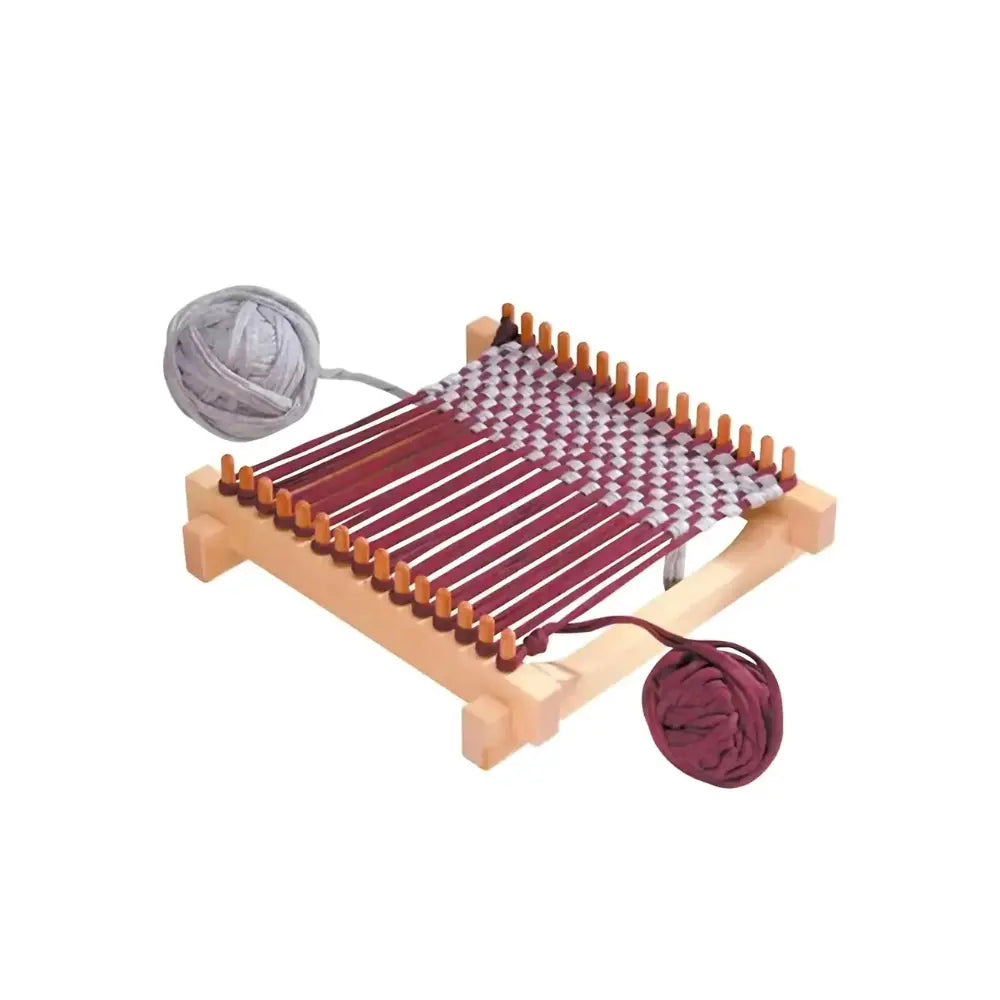 Small wooden weaving loom with a patterned fabric and two balls of yarn on a white background