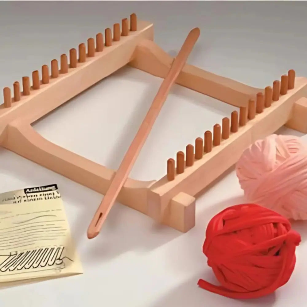 Wooden loom with a ball of red yarn and pink yarn on a light background