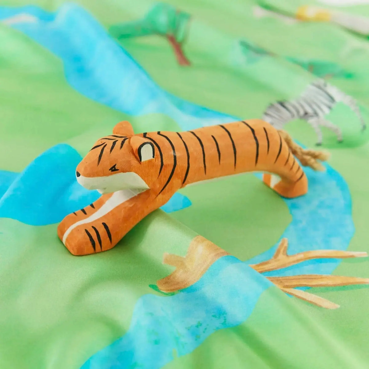 Wooden tiger toy resting on a colorful playmap playsilk