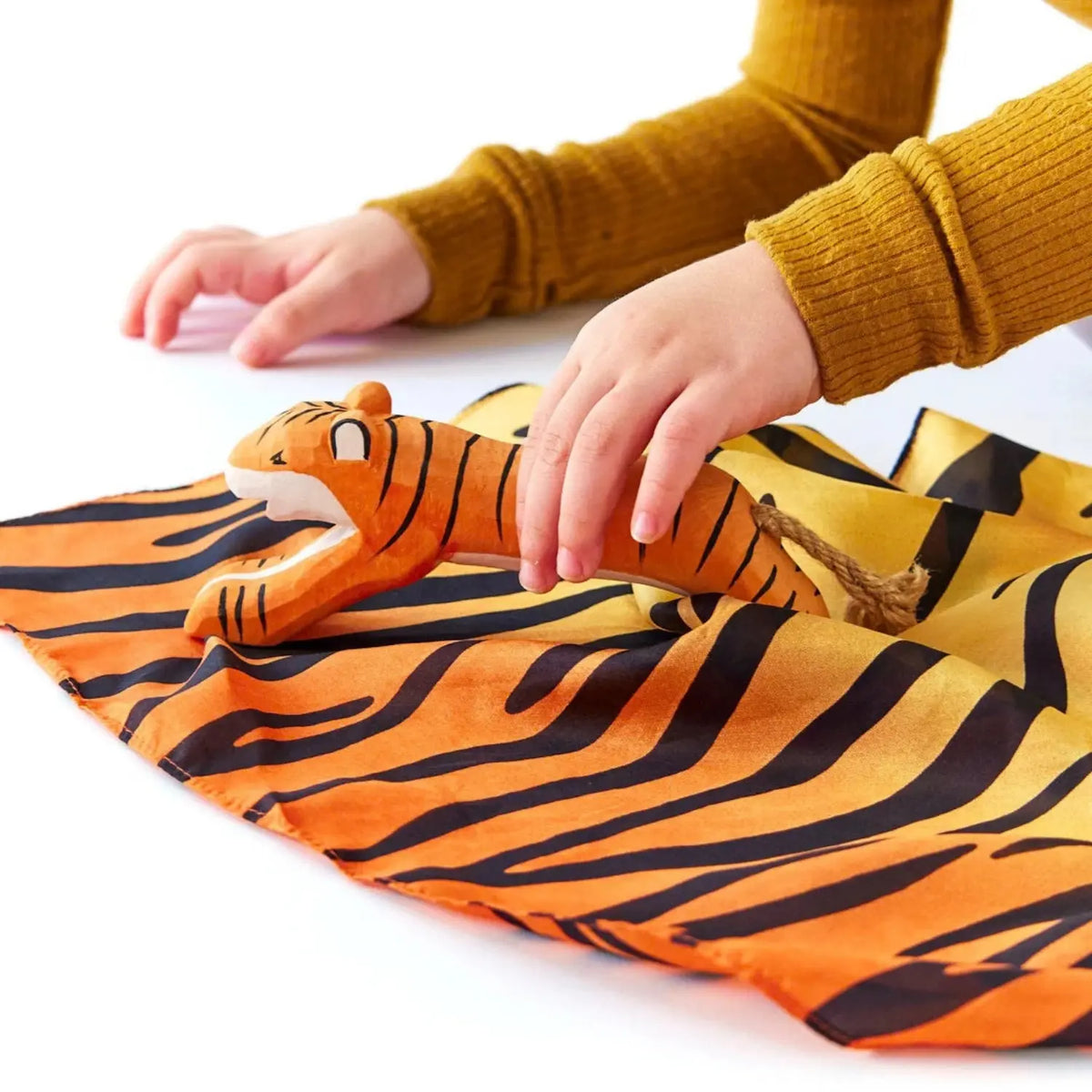Child arranges a wooden tiger on an orange tiger print playsilk