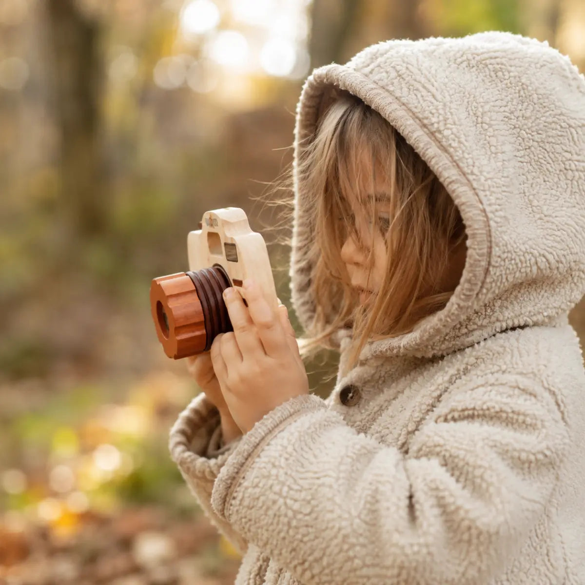 Side view of a wooden toy camera in use, showing how the interchangeable lens screws onto the camera