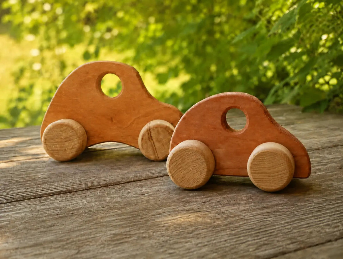 Two handmade wooden toy cars on a sunlit wooden porch for Waldorf-inspired play.