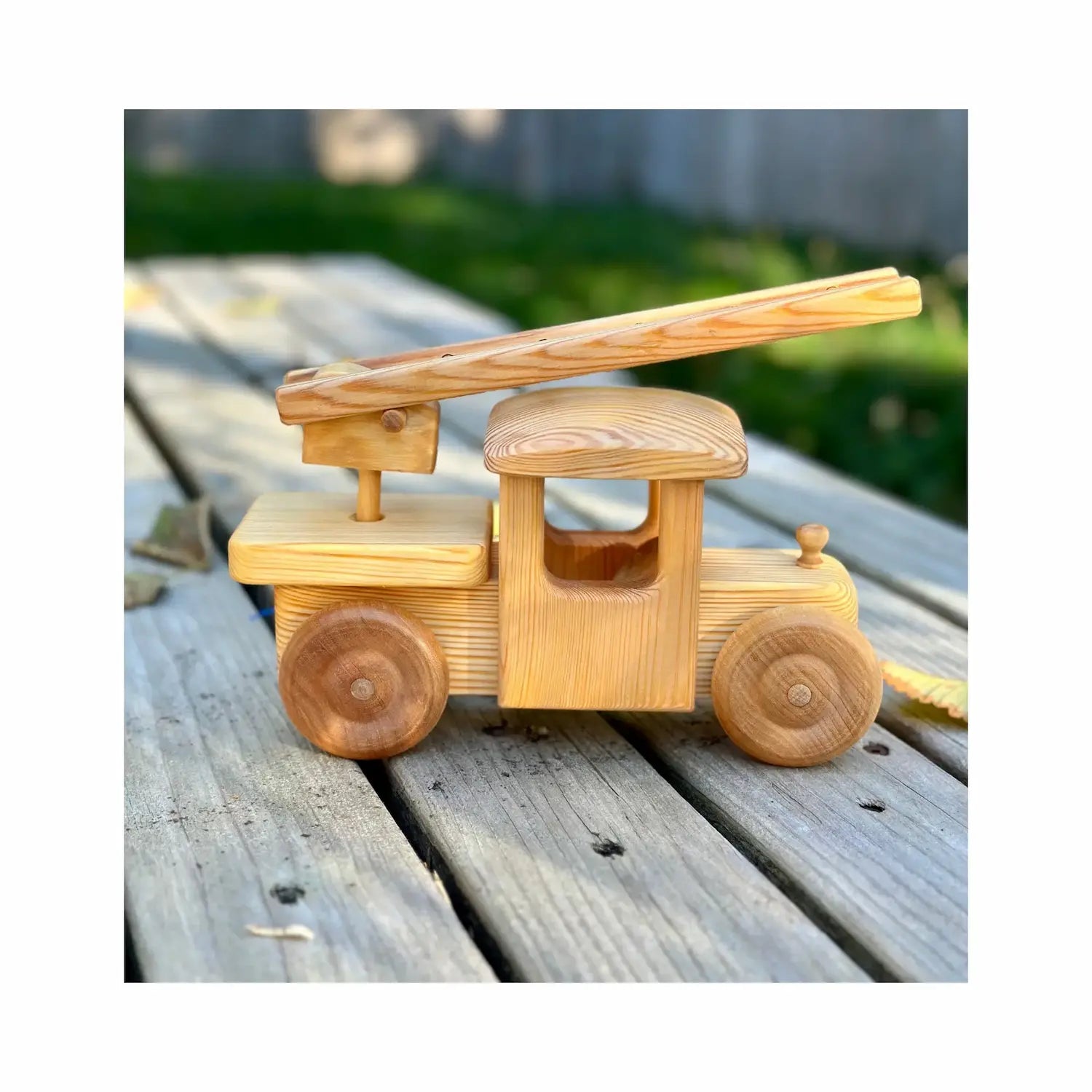 Wooden toy firetruck resting on outdoor surface showing side view with ladder
