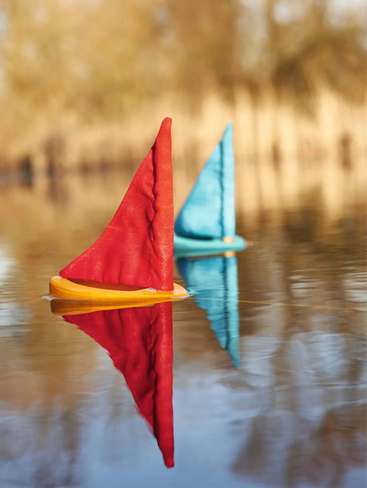 Two wooden toy sailboats floating on water showing bath and outdoor play use