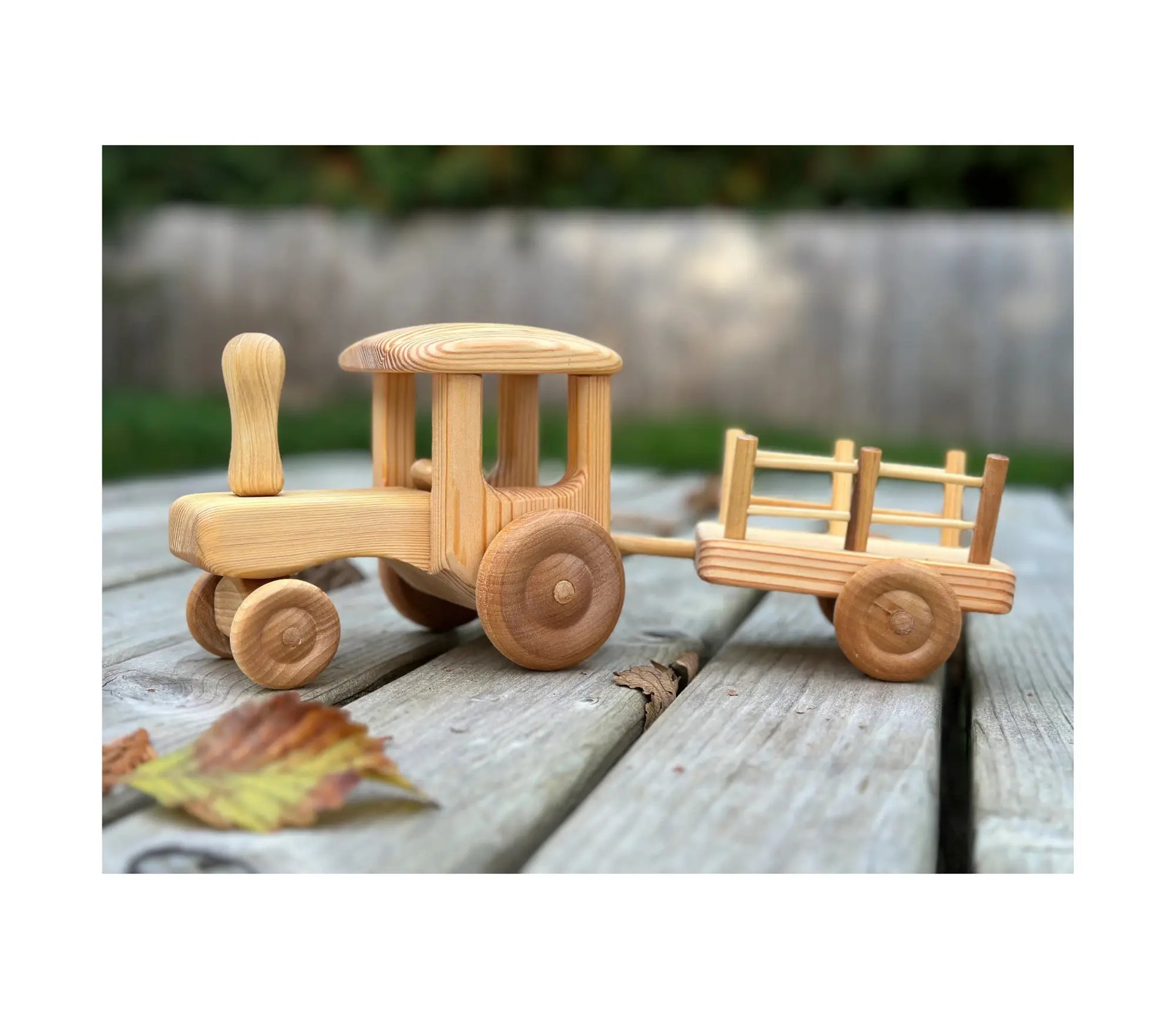 Wooden tractor with trailer shown from side angle outdoors on wooden surface with autumn leaves