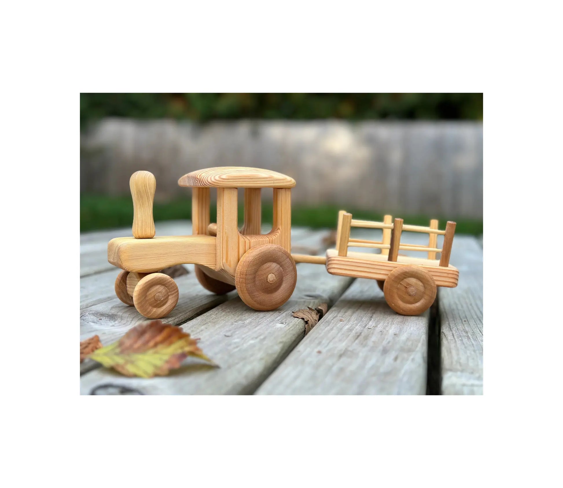 Wooden tractor with trailer by Telleby outdoors on wooden surface with autumn leaves showing natural play setting