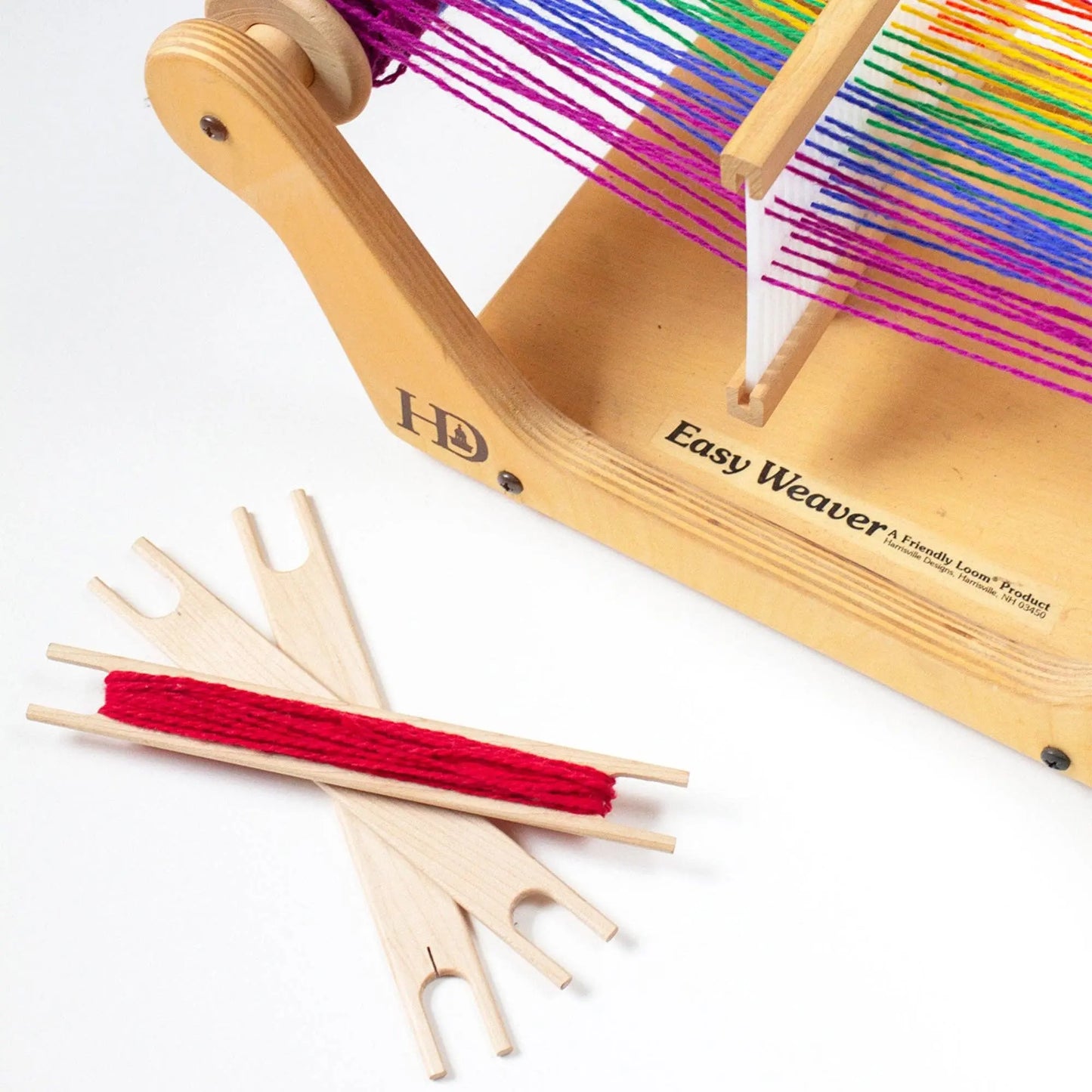 Close-up of wooden weaving loom with rainbow yarn and stick shuttles