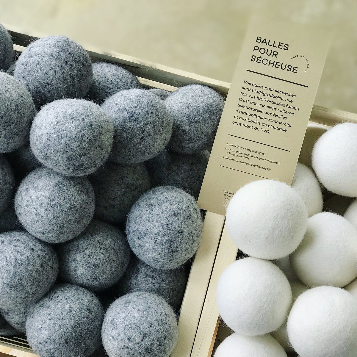 close up of gray and white wool dryer balls in wooden boxes with sign in French