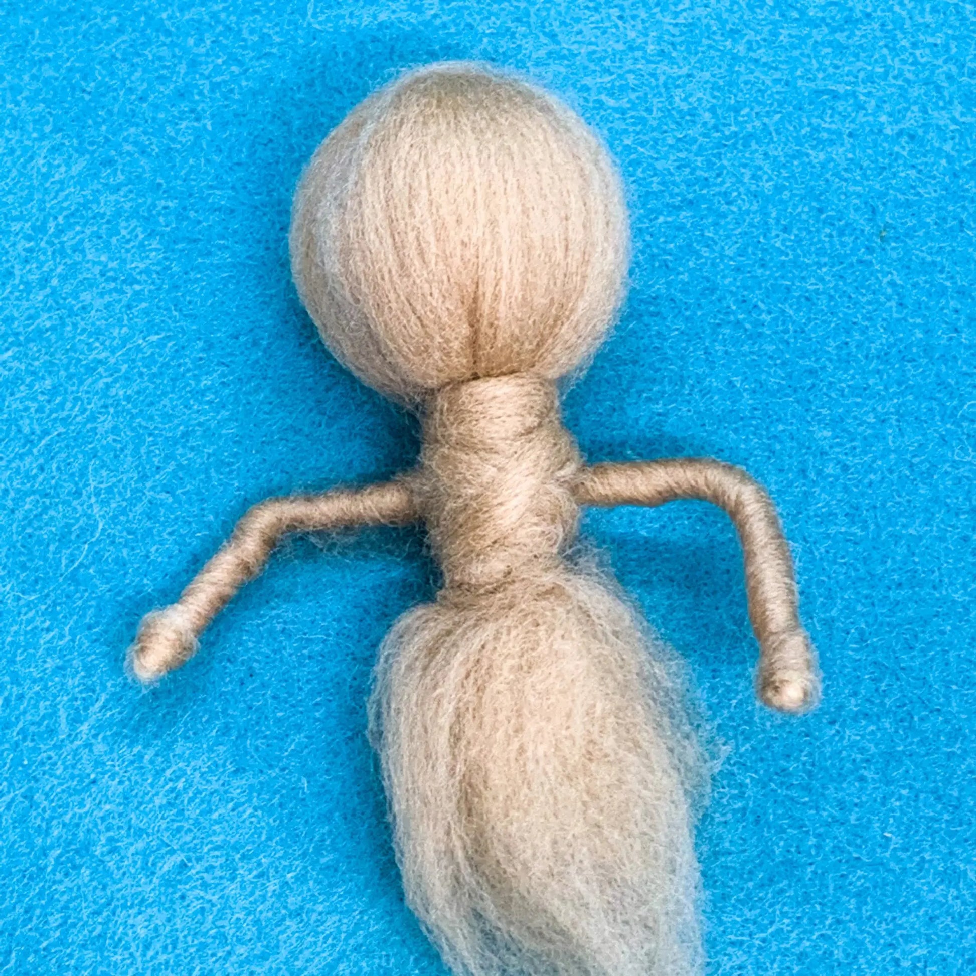 Textile art figure made from merino wool on a blue background