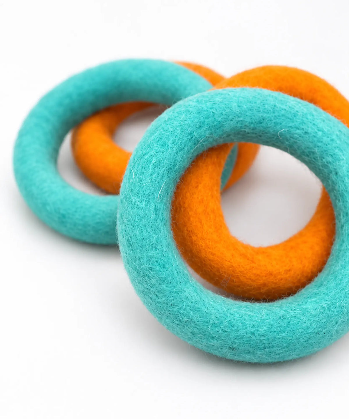 Two teal and two orange wool felt rings overlapping, showing their soft felted texture.