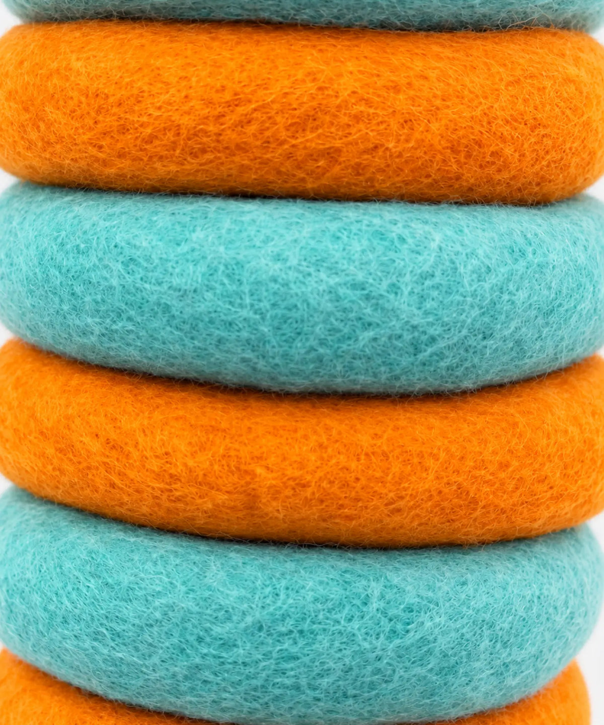 Close-up of stacked orange and teal wool felt rings showing the fine wool fibers.