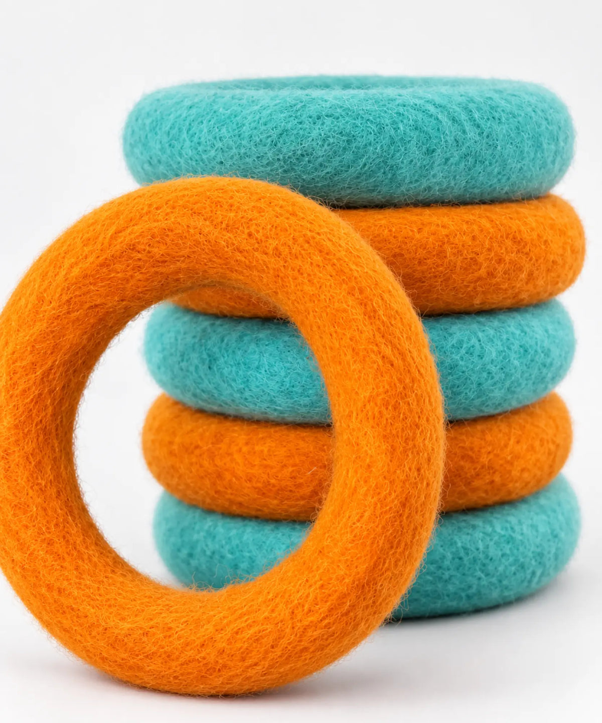 Orange and teal wool felt rings stacked with an orange ring leaning against the front.