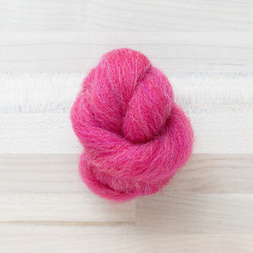 knot of wool roving in rhubarb pink for needle felting on a wooden background
